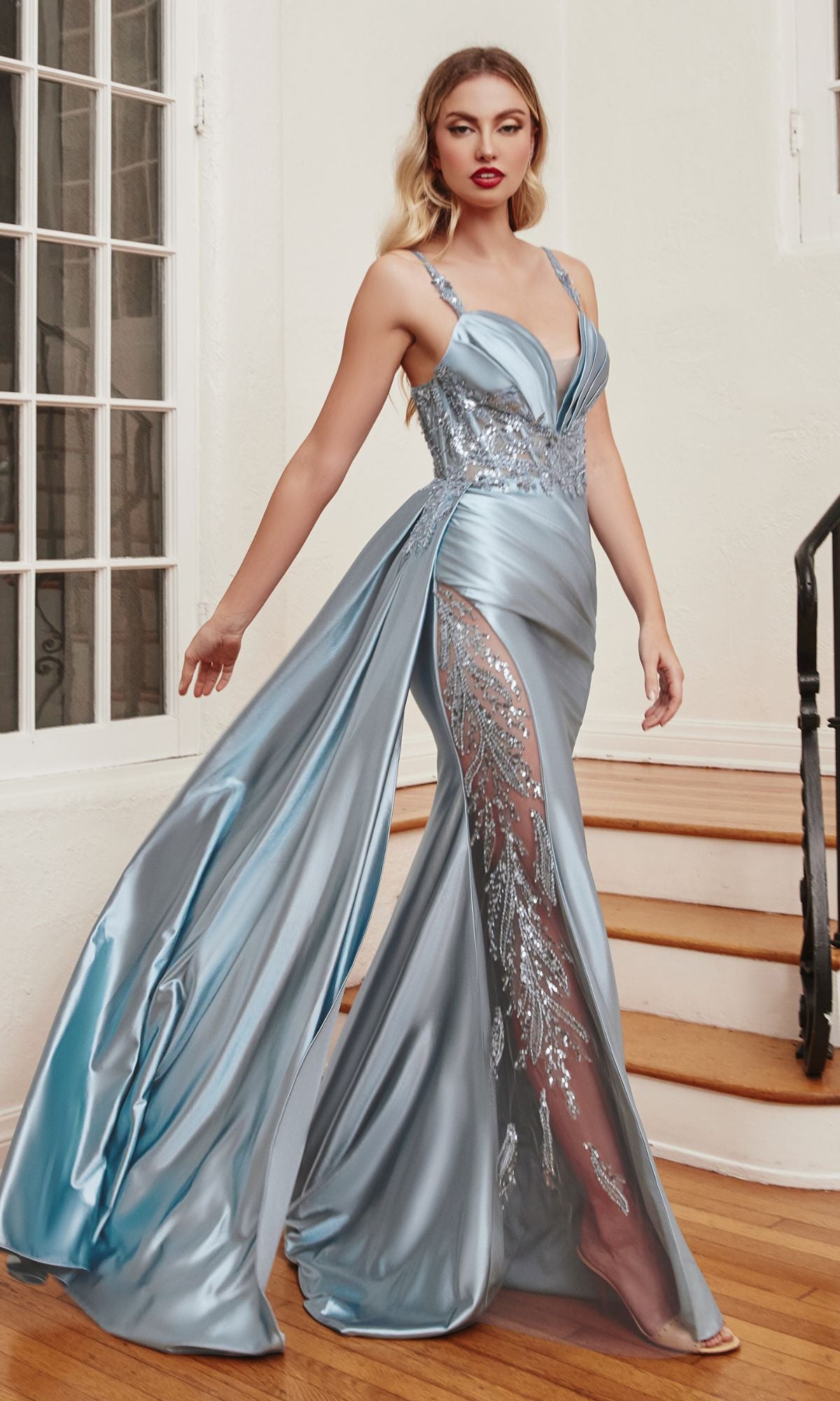 A woman stands indoors on a staircase wearing the Long Satin Formal Dress with Side Sash CDS417, a light blue, floor-length gown featuring sequin embellishments, lace details, and a high slit.